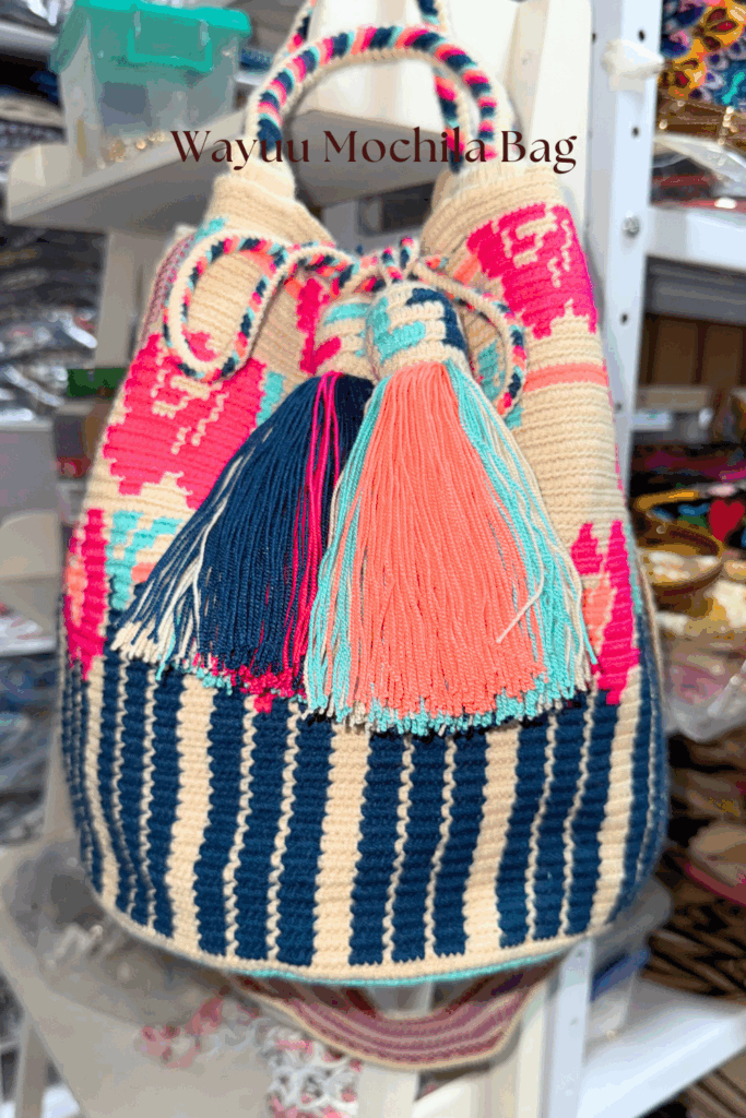 Authentic handmade Wayuu bag in beige base with vibrant blue and pink geometric patterns, crafted by Colombian artisans.
